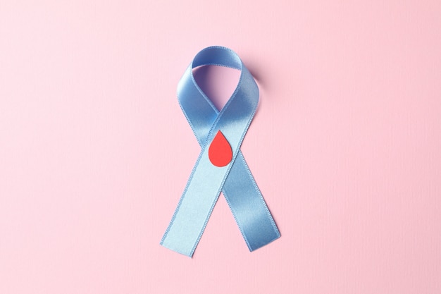 Diabetes. Cinta de conciencia azul con gota de sangre decorada sobre fondo rosa