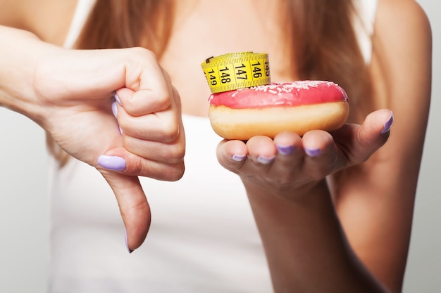 Diät. Donut Nr. Ein junges Mädchen hält einen Donut an der Hand und zeigt ihren Finger unten. Nicht süß. Makrophotokraten. Das Konzept der Gesundheit. Auf grauem Hintergrund.