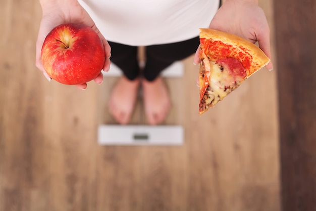 Foto diät. frauen-messendes körpergewicht auf der waage, die pizza hält.