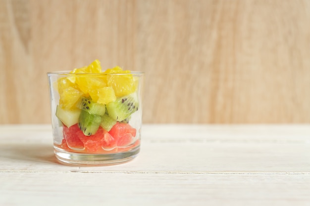 Diät-frischer geschmackvoller Mischungsobstsalat in einem Glasgefäß auf Holztisch. Gehackte saftige Orangen, Kiwi und Pampelmusen.