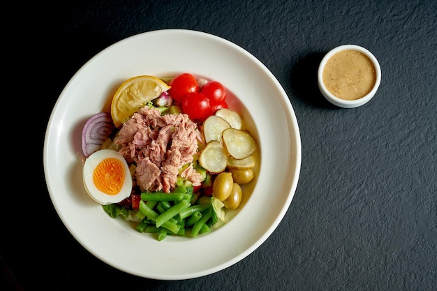 Diät-Nicoise-Salat mit Thunfisch, Ei und Spargel in einem weißen Teller auf schwarzem Hintergrund