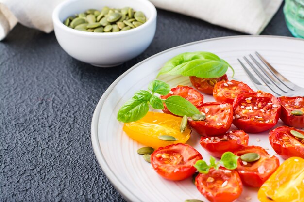 Diät-vegetarischer Snack. Sonnengetrocknete Tomaten mit Basilikum, Sesam und Kürbis auf einem Teller auf schwarzem Hintergrund. Nahaufnahme. Platz kopieren