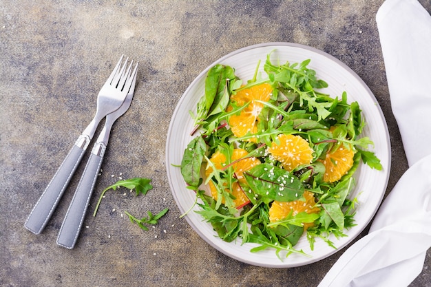 Diät-vegetarischer Vitaminsalat aus Orangenstücken und Mischung aus Rucola, Mangold und Mizun-Blättern auf einem Teller auf dem Tisch. Ansicht von oben