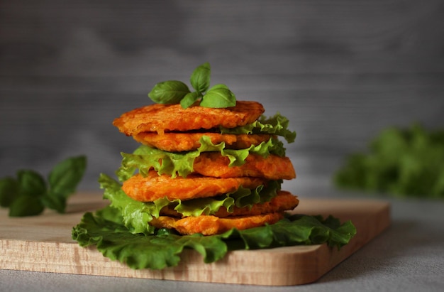 Diätetische natürliche Karottenpfannkuchen mit Salatblättern auf einem Holzbrett auf grauem Hintergrund