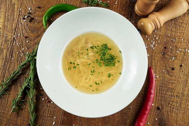 Foto diätetische suppe mit huhn, gemüse und petersilie in kompostion mit zutaten auf holzoberfläche in weißer schüssel. draufsicht leckere suppe. flaches essen