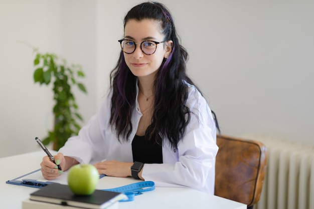 Foto diätetischer arzt mit laborkittel am tisch sitzend mit blick auf die kamera und lächelnd popularität einer gesunden und richtigen ernährung