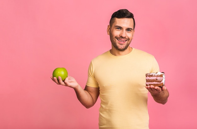 Diätkonzept. Junger Mann denkt, was zwischen einem Apfel und einem Kuchen zu essen ist