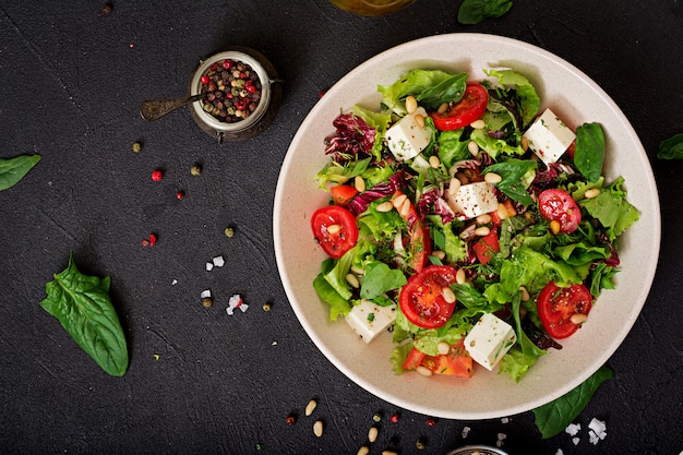 Foto diätsalat mit tomaten, feta, salat, spinat und pinienkernen. ansicht von oben. flach liegen.