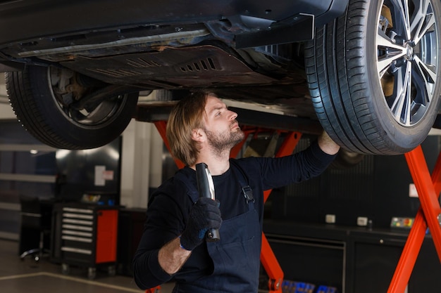 Diagnóstico de la suspensión y el sistema de frenos Un mecánico de automóviles con una linterna inspecciona el automóvil desde abajo