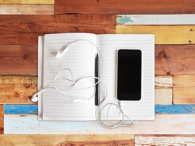 Diario en blanco con lápiz y teléfono inteligente con auriculares en una mesa de madera