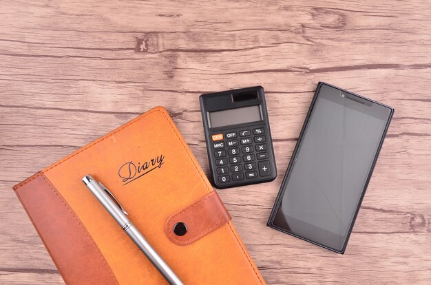 Diario con bolígrafo, teléfono inteligente y calculadora en mesa de madera