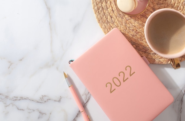 Foto diario de color rosa coral para el año bolígrafo café macarrón galleta sobre mantel tejido de paja