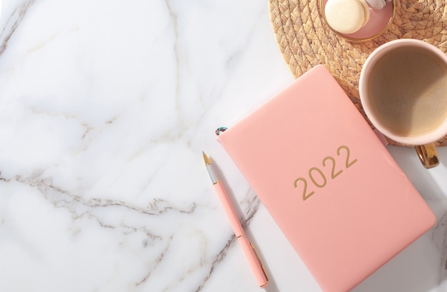 Foto diario de color rosa coral para el año bolígrafo café macarrón galleta sobre mantel tejido de paja