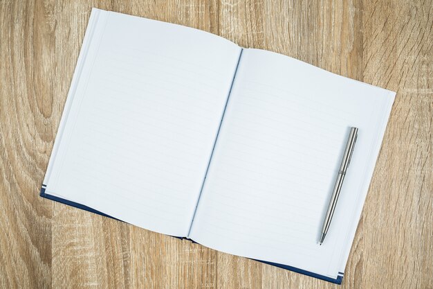 Foto diario de cuaderno en blanco con bolígrafo plateado sobre mesa de madera