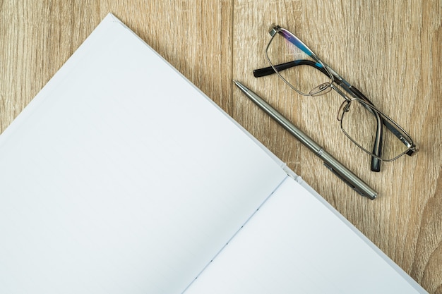 Diário de caderno em branco com caneta e óculos prateado