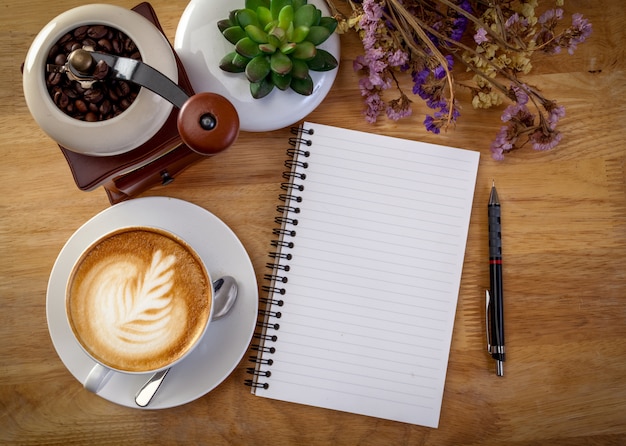 Diario, flor y taza de café en la mesa de madera.