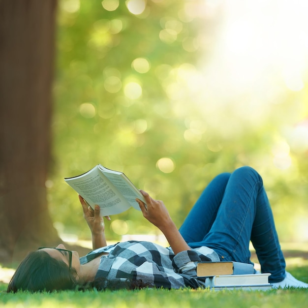 Dias de verão preguiçosos Foto de uma jovem deitada na grama e lendo um livro