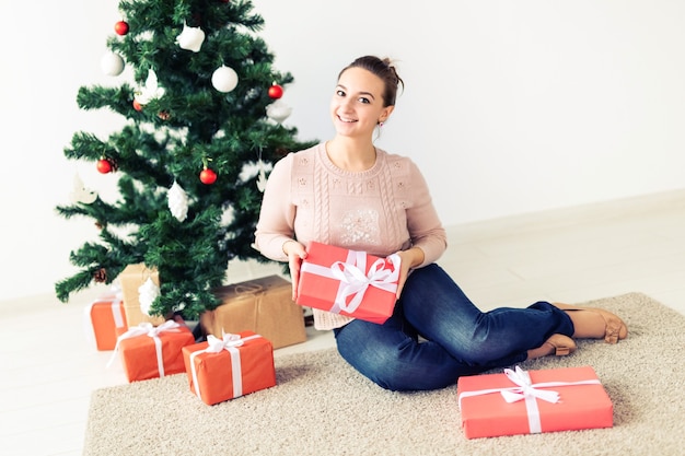 Días de fiesta, celebración y concepto festivo - Hermosa mujer joven sentada bajo el árbol de Navidad