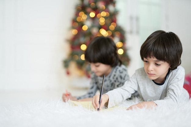 Días de invierno, dos niños latinos gemelos haciendo dibujos con lápices de colores mientras están acostados