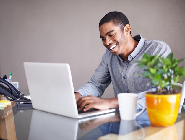 Uno de esos días en los que todo va sobre ruedas Foto de un apuesto joven felizmente trabajando en su computadora portátil en casa