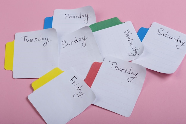 Los días de la semana las pegatinas de papel unidas al fondo rosa.