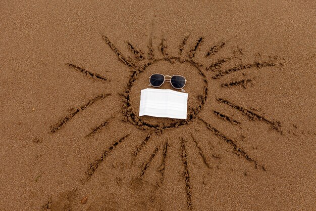 Dibujando gafas de sol y una mascarilla médica en la arena de la playa descansan en el mar y la costa durante el ...