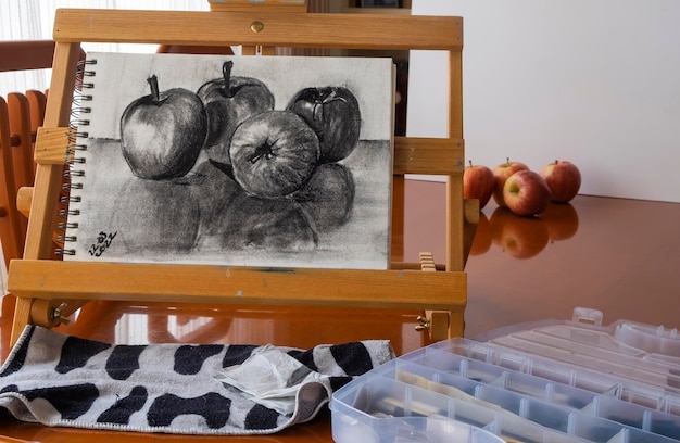 Dibujar frutas con carboncillo cuatro manzanas en un bloc de dibujo en un caballete portátil