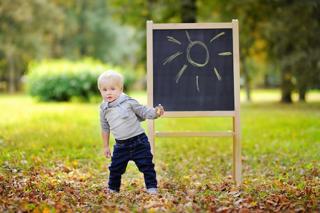 Dibujo hermoso del niño pequeño que hace una pausa una pizarra al aire libre