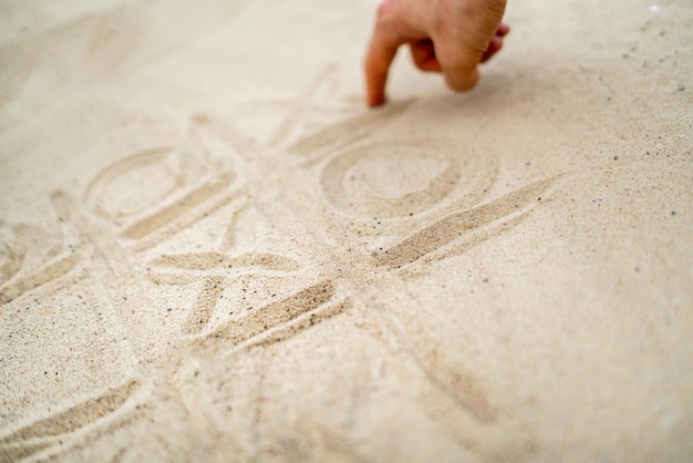 Dibujo a mano tres en raya jugando en la arena en la playa de verano