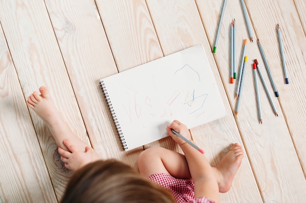 Dibujo de niña con lápices de colores sentado piso de madera.