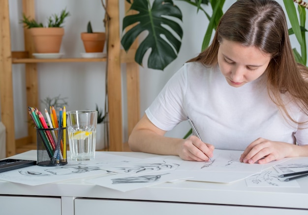 Los dibujos hechos a lápiz están sobre la mesa Una mujer joven de apariencia europea dibuja con un lápiz sobre papel blanco Gráficos El proceso de dibujar con un lápiz en casa en una mesa blanca