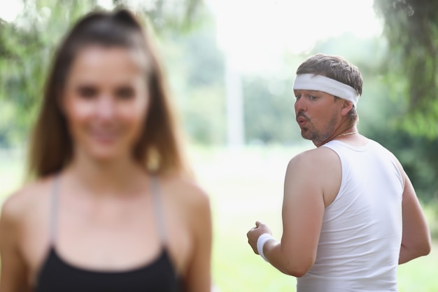 Dicker Mann in der Sportbekleidung, die junges Mädchen betrachtet, das im Park joggt