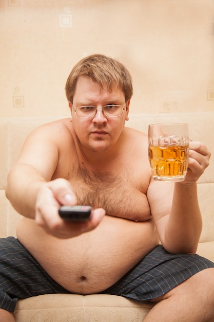 Dicker Mann mit Bierbauch vor dem Fernseher isst Popcorn und trinkt Bier