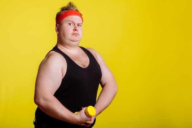 Dicker Mann mit Hantel auf gelber Wand. Motivation für dicke Leute