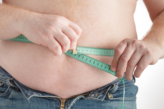 Dicker Mann überprüft sein Körperfett mit Maßband auf Fett oder Fettleibigkeit