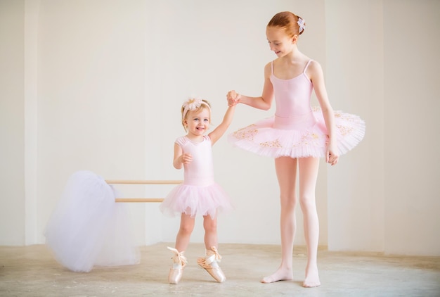 Foto die ältere schwester, eine ballerina in einem rosa tutu und spitzenschuhen, zeigt dem baby, wie man an der barre übt