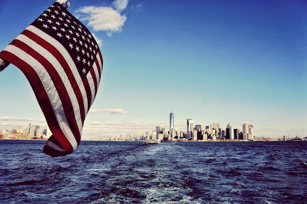 Die amerikanische Flagge schwingt über dem Fluss mit städtischer Skyline im Hintergrund