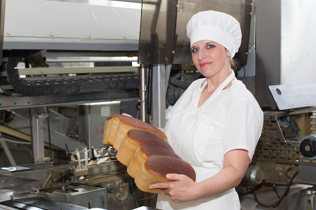 Die Arbeiterin der Fabrik zur Herstellung von Brot mit Brot in ihren Händen.Brotfabrik mit einem Arbeiter