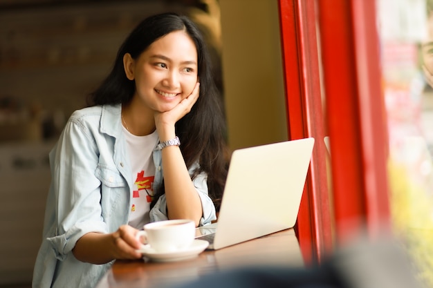 Die Asiatin, die Laptopfunktion verwendet und trinken Kaffee im Café