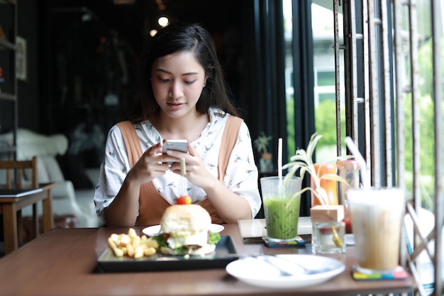 Die asiatinnen, die foto von hamburgern machen und genossen, am kaffee und am restaurant zu essen, entspannen an sich zeit