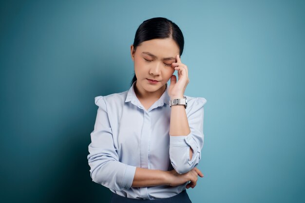 Die asiatische Frau hatte Kopfschmerzen und berührte ihren Kopf isoliert auf Blau.