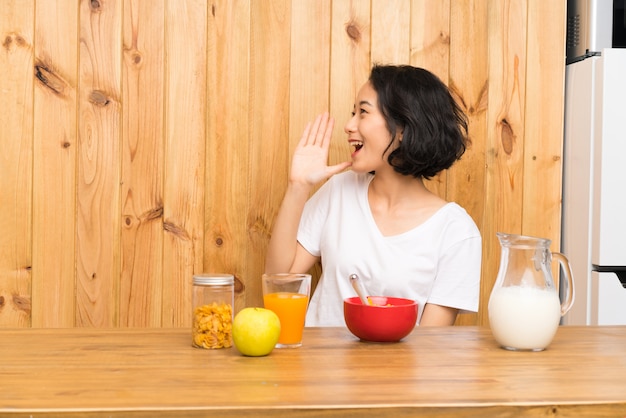 Die asiatische junge Frau, die Frühstücksmilch schreit mit dem breiten Mund hat, öffnen sich