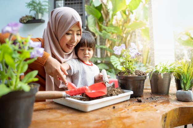 Die asiatische Mutter hilft ihrer Tochter, mit einer kleinen Schaufel aus einem Tablett Erde zu pflanzen, um Medien zu pflanzen