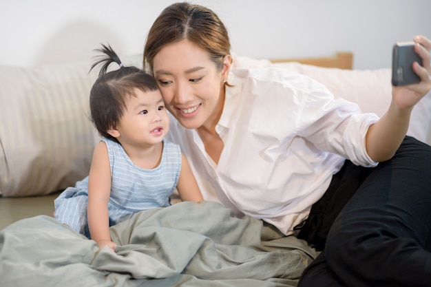 Die asiatische Mutter und ihre kleine Tochter telefonieren mit dem Vater im Bett.