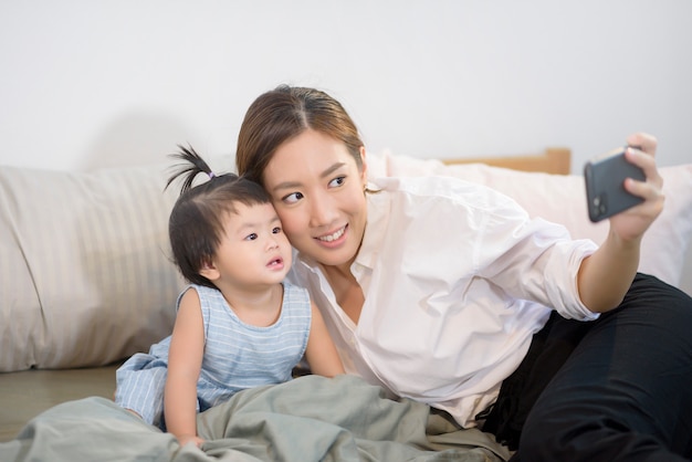 Die asiatische Mutter und ihre kleine Tochter telefonieren mit dem Vater im Bett.