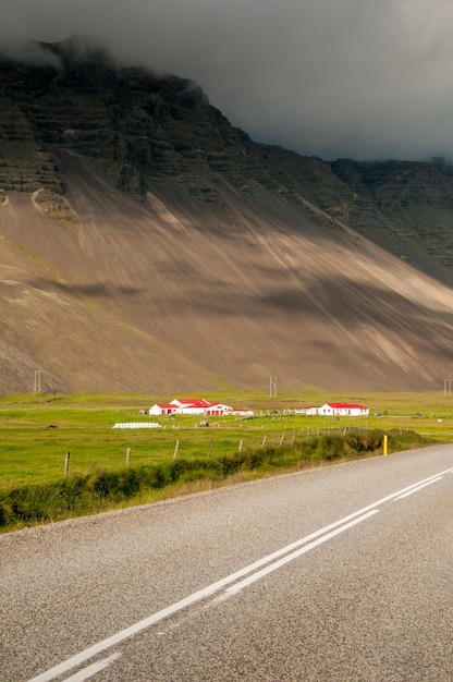 Die asphaltierte Straße Nummer 1 eine Wiese ein Bauernhof mit roten Dächern und ein von Wolken verdeckter Berg