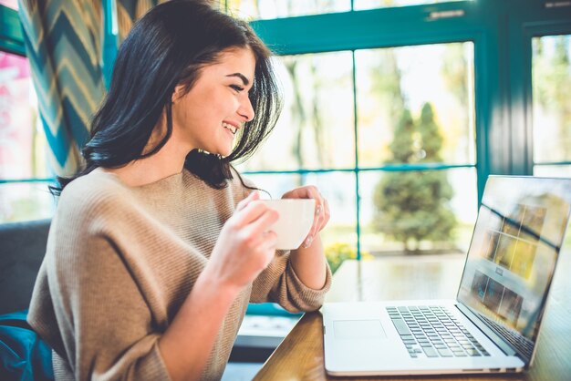 Die attraktive Frau mit Laptop trinkt einen Kaffee im Café