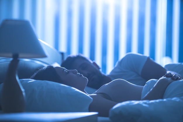 Die attraktive Frau schläft in der Nähe eines Mannes im bequemen Bett. Nachtzeit