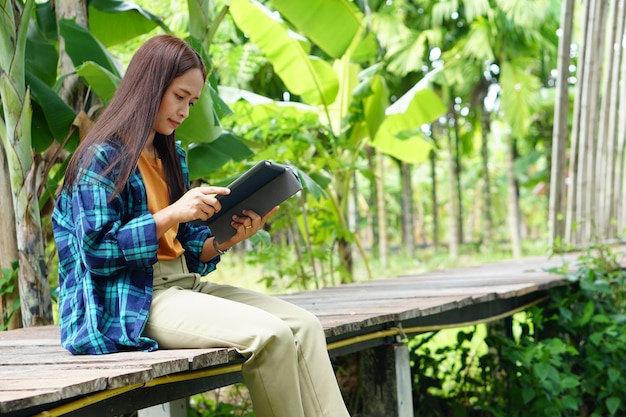 Die Bäuerin sitzt auf einer Holzbrücke und betrachtet die Ergebnisse einer Bananenplantage auf einem Laptop