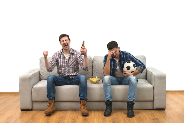 Die beiden Jungs mit Bier und Pommes schauen sich auf dem Sofa einen Fußball an